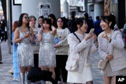 La gente espera en fila cerca de un cartel para tomarse fotografías, mientras otros, a la derecha, reaccionan a su selfie antes del concierto de Taylor Swift en el Tokio Dome en Tokio, el sábado 10 de febrero de 2024. (Foto AP/Hiro Komae)