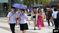 Para pejalan kaki menggunakan payung untuk melindungi dari panas sinar matahari di mal Siam Paragon, Bangkok, 1 April 2024. (Foto: Lilian Suwanrumpha/AFP)