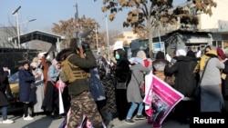 FILE - A member of Taliban forces fires in the air to disperse the Afghan women during a rally to protest against what the protesters say is Taliban restrictions on women, in Kabul, Dec. 28, 2021. 