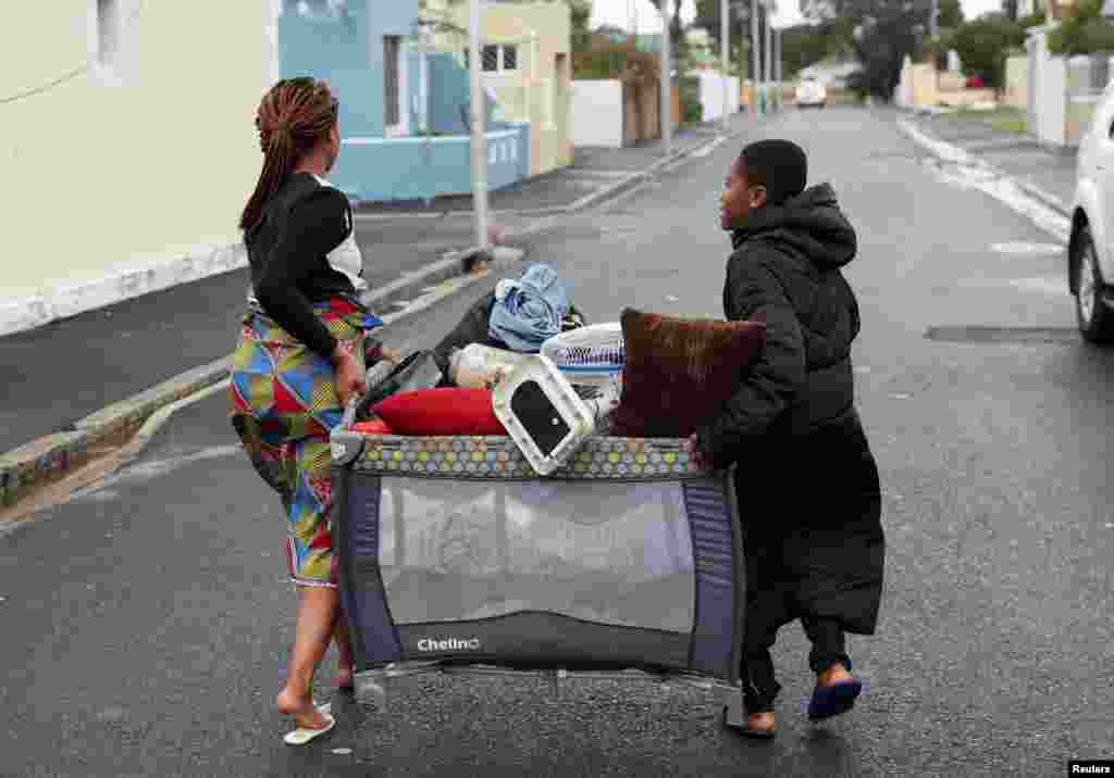 Dua warga membawa barang-barang mereka ke tempat aman setelah angin kencang meniup atap dan merusak rumah mereka selama cuaca dingin di Wynberg, Cape Town, Afrika Selatan. (Reuters)&nbsp;