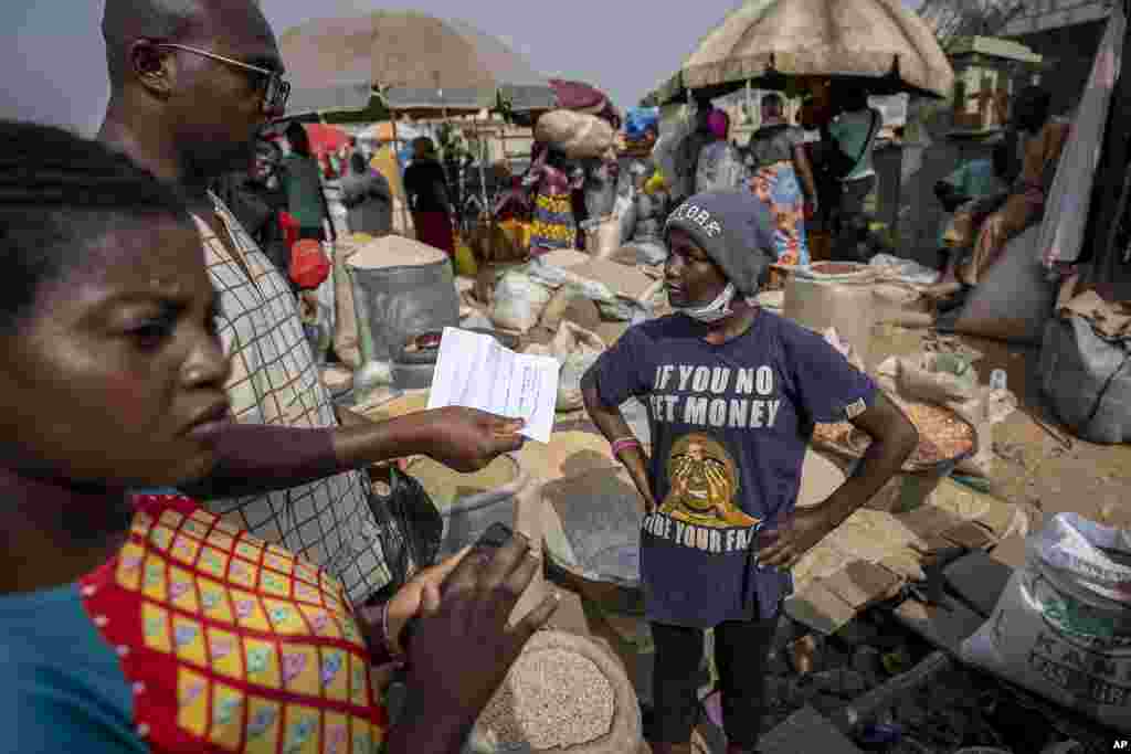 A customer buying a small bag of melon seeds discusses how he will send a bank transfer to the street seller, right, due to the crisis in the supply of banknotes, at the bi-weekly Karmo street market in Abuja, Nigeria Tuesday, February 28, 2023.&nbsp;