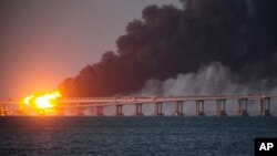 Api dan asap mengepul dari arah jembatan Kerch yang menghubungkan wilayah daratan Rusia dengan Semenanjung Krimea di Kerch, Krimea, pada 8 Oktober 2022. (Foto: AP)