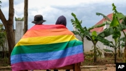 FILE - A gay Ugandan couple cover themselves with a pride flag as they pose for a photograph in Uganda Saturday, March 25, 2023. 