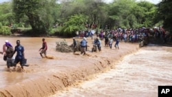 People cross through a flooded Muuoni River, where eight people are said to have drowned overnight while crossing the river at Mukaa area, Makueni county, eastern Kenya on Friday, November 24, 2023.