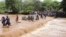 People cross through a flooded Muuoni River, where eight people are said to have drowned overnight while crossing the river at Mukaa area, Makueni county, eastern Kenya on Friday, November 24, 2023.