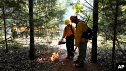 Student Kolin Bilbrew, left, starts a prescribed fire with instructor James Klungness-Mshoi, right, during a wildland firefighter training, June 9, 2023, in Hazel Green, Alabama.