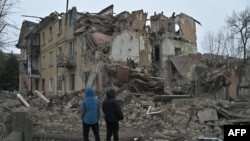 Local residents stand among debris of a residential building partially destroyed by a missile attack in the town of Selydove, Donetsk region, Ukraine, on Feb. 8, 2024.