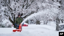 FILE - A person removes snow from a sidewalk during a winter storm in Doylestown, Pa., Feb. 13, 2024. 