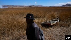 An Aymara man walks past an abandoned boat near the shore of Lake Titicaca in Huarina, Bolivia, on July 27, 2023. The lake's low water level is affecting local communities that rely on the natural border between Peru and Bolivia for their livelihood.
