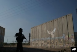 A member of Israeli forces stands next to a security wall with Hebrew writing reading "Path to Peace" at the Kibbutz Netiv Haasara near the border with Gaza Strip, Israel, Nov. 17, 2023.