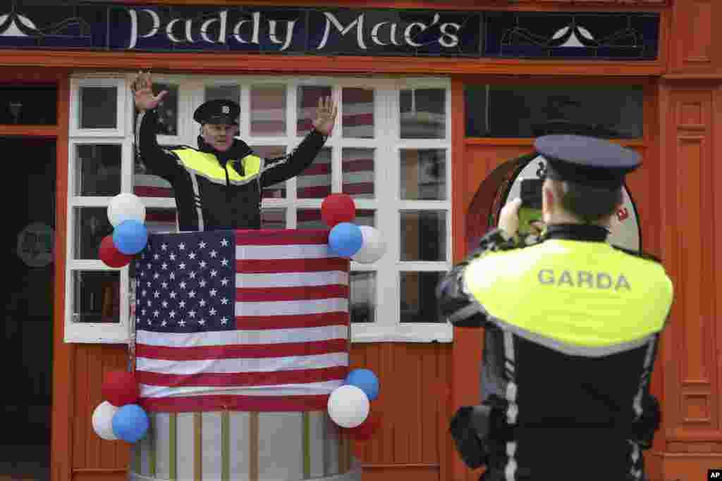 Seorang polisi Irlandia berpose saat rekannya memotretnya dengan latar belakang bendera AS yang dipasang di kota Ballina, menjelang kunjungan Presiden Joe Biden ke Katedral St Muredach, di Ballina, Irlandia.