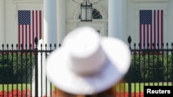 Seorang perempuan mengenakan topi memperhaitkan bendera yang menghiasi North Portico Gedung Putih saat liburan hari kemerdekaan Amerika Serikat, Senin, 3 Juli 2023. (Foto: Kevin Lamarque/Reuters)