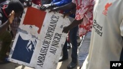 Des manifestants tiennent une pancarte arrachée à l'ambassade de France à Niamey lors d'une manifestation qui a suivi un rassemblement de soutien à la junte nigérienne à Niamey le 30 juillet 2023.