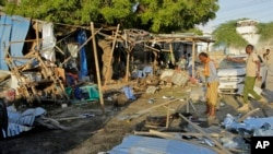 People stand near the wreckage of a car and kiosks after a bombing in Mogadishu, Somalia, Sept. 29, 2023.