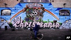 FILE - A man rides a bicycle by The Grey Hall at Christiania neighborhood of Copenhagen, Feb. 11, 2004. 