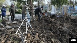 Workers clean a graveyard in the region of Donbass after the cemetery was shelled during the Russian invasion of Ukraine, April 11, 2023.