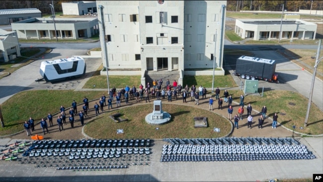 In this photo from the Defense Advanced Research Projects Agency, drones and participants in a Defense Department urban warfare exercise pose at Fort Campbell, Tenn., on Nov., 2021. A single operator supervised a swarm of more than 100 drones at the exercise. (DARPA via AP)