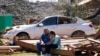 FILE - Charles Shields, left, sits with friend Robbie Diffey on the roof of Diffey's garage after a tornado destroyed her home, March 27, 2023, in Rolling Fork, Miss. President Joe Biden on Friday will visit the town.