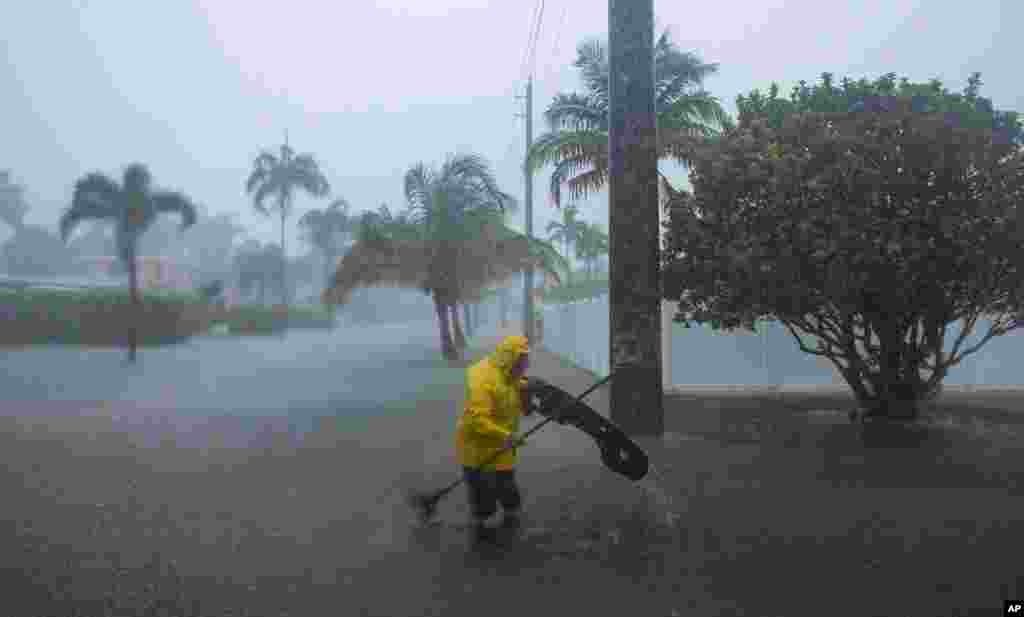 Un hombre trabaja para limpiar los escombros de una calle inundada mientras cae fuerte lluvia en Hollywood, Florida.