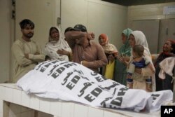 Orang-orang berduka di samping jenazah seorang kerabat yang tewas dalam insiden desak-desakan di pusat distribusi makanan selama bulan Ramadan di Karachi, Pakistan, 31 Maret 2023.
