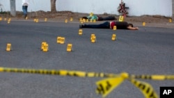 ARCHIVO - En esta fotografía de archivo del 29 de junio de 2017, los investigadores marcan el lugar donde cayeron casquillos de bala junto a varios cuerpos tirados en una carretera en la ciudad de Navolato, estado de Sinaloa, México.