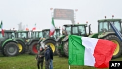 Bendera nasional Italia berkibar di depan traktor yang diparkir di sepanjang jalan saat para petani melakukan aksi protes di dekat pintu masuk jalan raya di Melegnano, dekat Milan, 30 Januari 2023. (GABRIEL BOUYS / AFP)