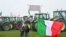 Bendera nasional Italia berkibar di depan traktor yang diparkir di sepanjang jalan saat para petani melakukan aksi protes di dekat pintu masuk jalan raya di Melegnano, dekat Milan, 30 Januari 2023. (GABRIEL BOUYS / AFP)