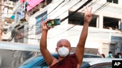 FILE - A Buddhist monk carrying a smart phone flashes a three-fingered salute in a gesture of solidarity as protesters march in Yangon, Myanmar, Feb. 7, 2021. Myanmar’s military government has launched an effort to block free communication on the internet.