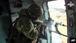 In this photo taken from video released by the Russian Defense Ministry Press Service on Dec. 28, 2023, a Russian soldier fires from aboard of a helicopter on a mission in Ukraine. 