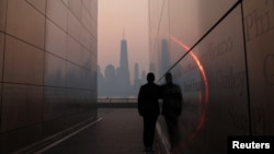 A man stands in the Empty Sky 911 Memorial in Jersey City, N.J., looking toward the One World Trade Center tower in New York City shortly after sunrise as haze and smoke caused by wildfires in Canada hangs over the Manhattan skyline, June 8, 2023. 