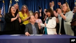 State officials applaud Colorado Gov. Jared Polis after he signed the first of three bills that enshrined protections for abortion and gender-affirming care, April 14, 2023, in the State Capitol in Denver.