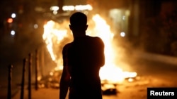 A person stands near a burning container as people protest following the death of Nahel, a 17-year-old teenager killed by a French police officer in Nanterre during a traffic stop, and against police violence, in Paris, France, June 30, 2023. 