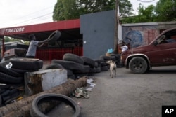 FILE - A man throws a tire to make a barricade to close a street at 6 p.m. as part of an initiative to fight gangs seeking to take control of their neighborhood in the Canape Vert area of Port-au-Prince, Haiti, May 31, 2023.
