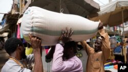 People balance a bag containing grains on a man's head at a market in Kano, Nigeria, July 13, 2023.