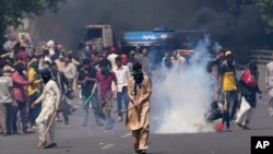 FILE - Supporters of Pakistan's former Prime Minister Imran Khan remove tear gas shell fired by police to disperse them during a protest in Lahore, Pakistan, May 10, 2023.