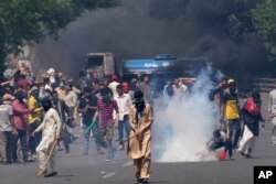 FILE - Supporters of Pakistan's former Prime Minister Imran Khan remove tear gas shell fired by police to disperse them during a protest in Lahore, May 10, 2023.