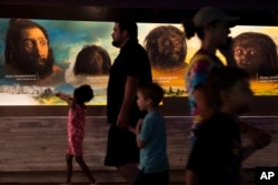 People walk past the faces of human ancestors as they visit the exhibits inside the Smithsonian Hall of Human Origins, July 20, 2023, at the Smithsonian Museum of Natural History in Washington.