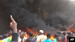 With the headquarters of the ruling party burning in the back, supporters of mutinous soldiers demonstrate in Niamey, Niger on Thursday, July 27 2023. 