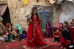 Shamila, 15, from an internally displaced family, adjusts her wedding dress in an old mud house yard, on her wedding day, on the outskirts of Kabul, Afghanistan, Friday, May 19, 2023. (AP Photo/Ebrahim Noroozi)