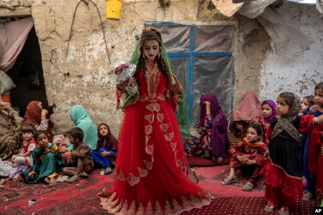 Shamila, 15, from an internally displaced family, adjusts her wedding dress in an old mud house yard, on her wedding day, on the outskirts of Kabul, Afghanistan, Friday, May 19, 2023. (AP Photo/Ebrahim Noroozi)