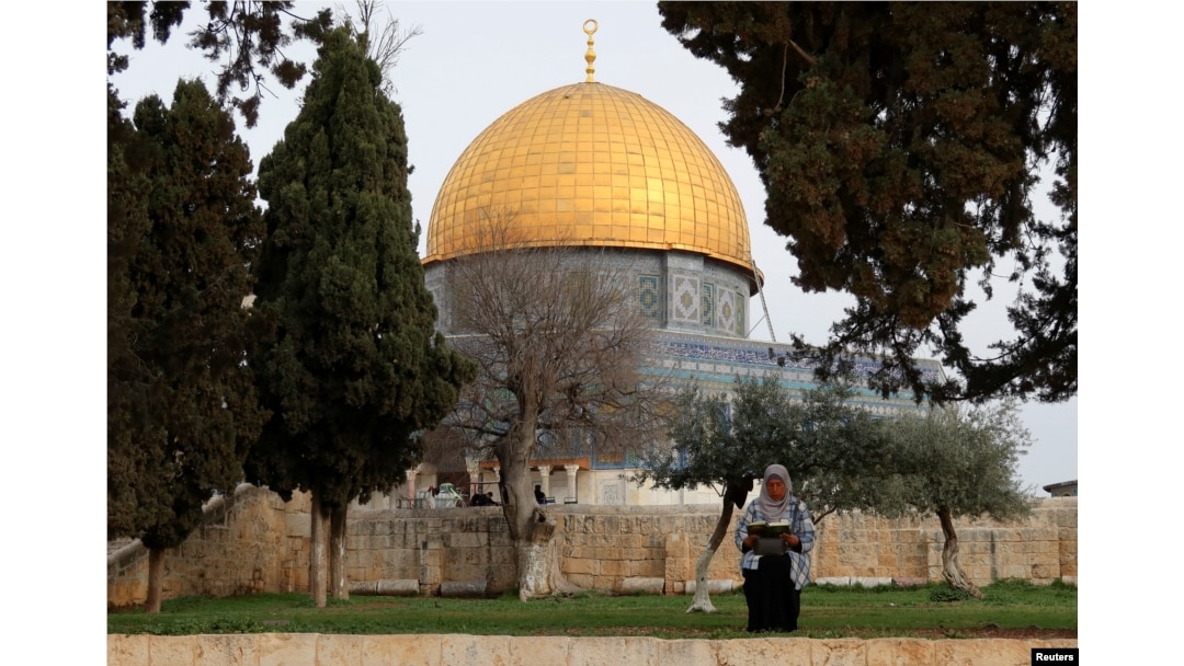 FILE - A Palestinian woman reads the holy book of Koran in the compound known to Muslims as the Noble Sanctuary and to Jews as the Temple Mount, in front of the Dome of the Rock, March 23, 2023.