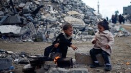 Dua anak Palestina menghangatkan diri dekat api di samping puing-puing rumah yang hancur akibat serangan Israel di Khan Younis di Jalur Gaza selatan, 27 November 2023.