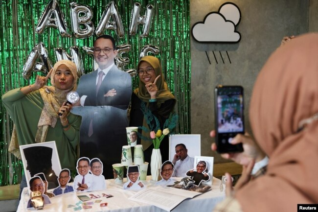 Perempuan berpose untuk foto dengan potongan foto calon Presiden Anies Baswedan saat Acara Humanies Cup Sleeve di kafe Kopi Nako di Jakarta, 4 Februari 2024. (REUTERS/Ajeng Dinar Ulfiana)