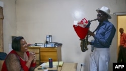 Musician and saxophonist Arundel Matoi, known as Sir Arundel, serenades Tarisai Leoba (R) as he delivers a "money bouquet" on Valentine's Day where his musical accompaniment is part of a suprise romantic gift at the ladies work offices in Harare on February 14, 2024. 