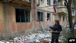 Жена стои близу зградатата каде што живее која е оштетена за време на ноќен напад во градот Селидове, регион Доњецк, Украина, на 14 април 2024 година.