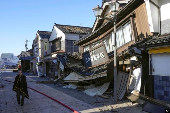 People walks past a collapsed houses following an earthquake in Wajima, Ishikawa prefecture, Japan Tuesday, Jan. 2, 2024. (Kyodo News via AP)