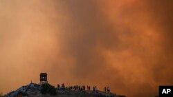 Orang-orang menyaksikan kebakaran hutan yang tidak terkendali di Mandra sebelah barat ibu kota Athena, Yunani di tengah gelombang panas esktrem yang melanda Eropa hari Selasa, 18 Juli 2023. 