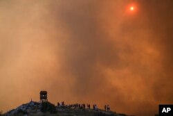 Orang-orang menyaksikan kobaran api kebakaran hutan yang belum bisa dikendalikan di kota Mandra sebelah barat Athena, Yunani, 18 Juli 2023.