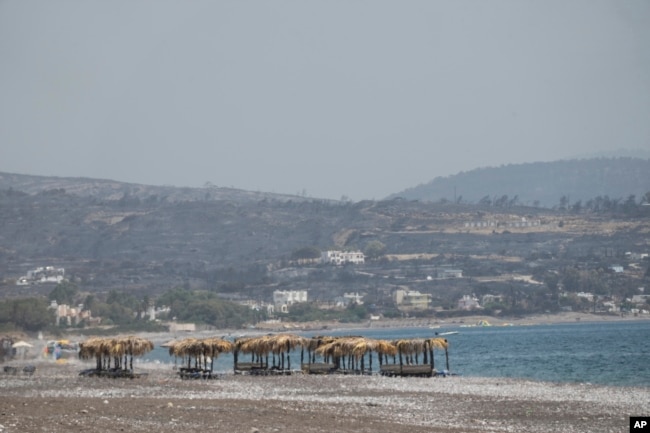 Abandoned sunbeds and umbrellas stand at the beach as a burnt hill is seen in the background after a wildfire, near Gennadi village, on the Aegean Sea island of Rhodes, southeastern Greece, July 27, 2023.