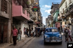 People walk under a sign announcing a private grocery store, left, in Havana on Nov. 11, 2023.